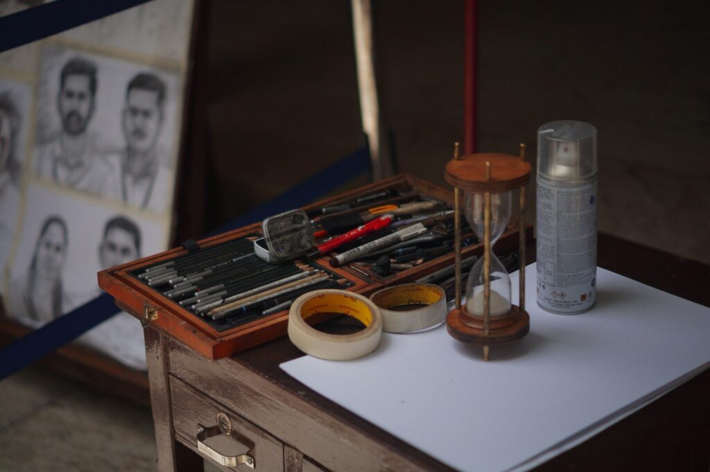 Art supplies, hourglass, and portraits sit on a table.